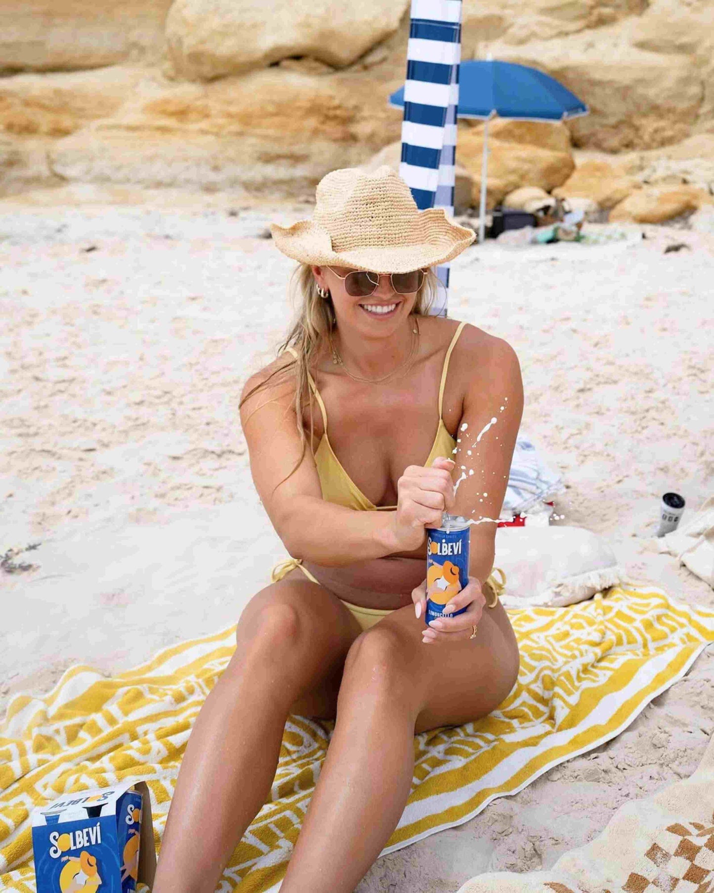 Woman in yellow swimsuit and hat enjoying Solbevi Limoncello Spritz by the beach