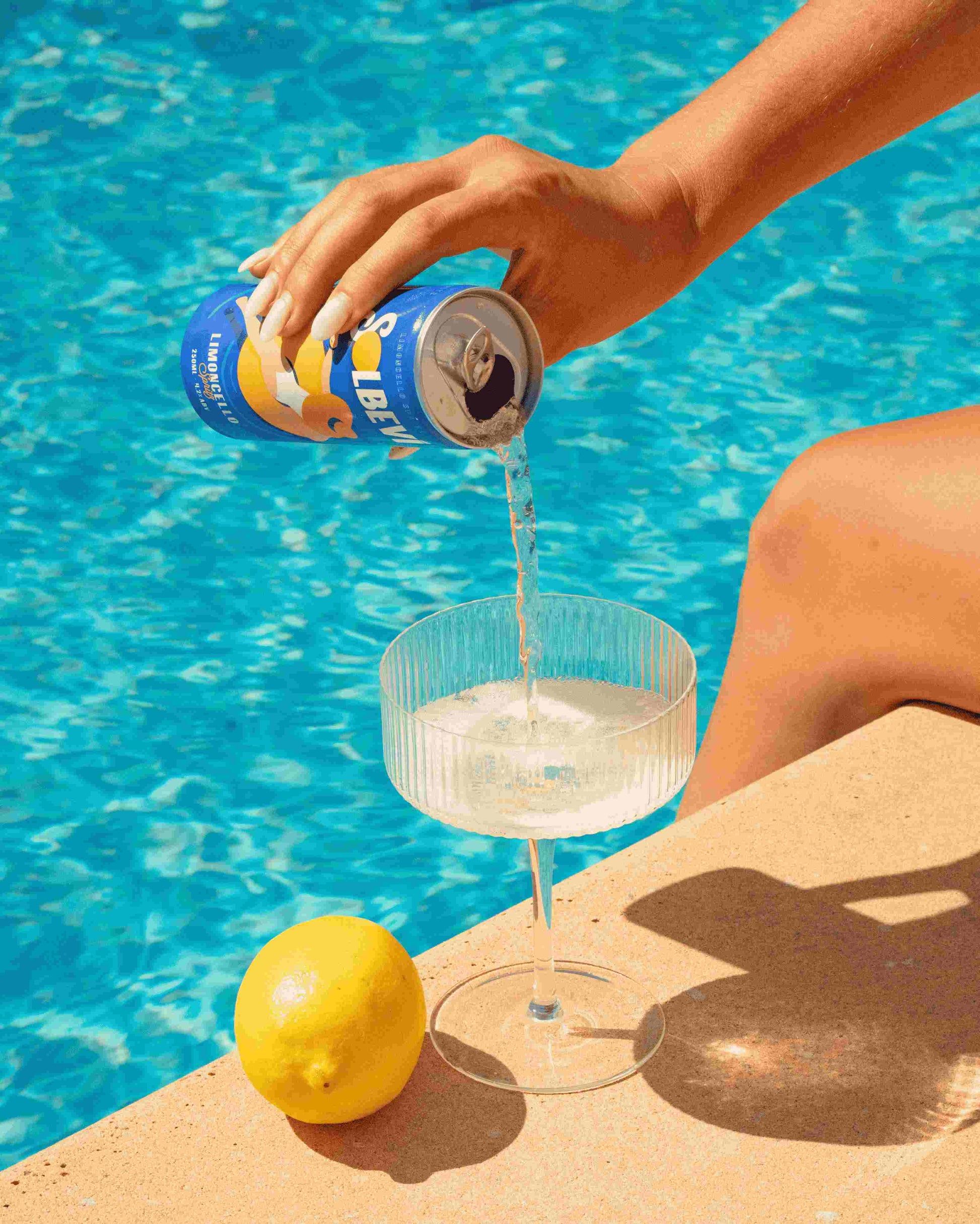 Woman pouring Solbevi Limoncello Spritz into a glass by the pool