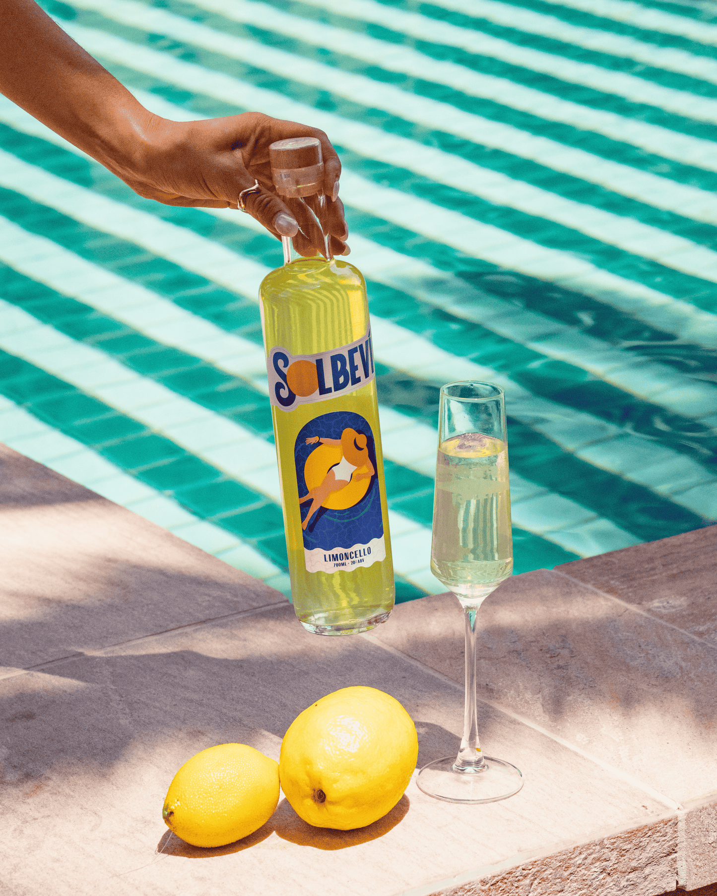 Solbevi Limoncello bottle beside fresh lemons and glasses by the pool